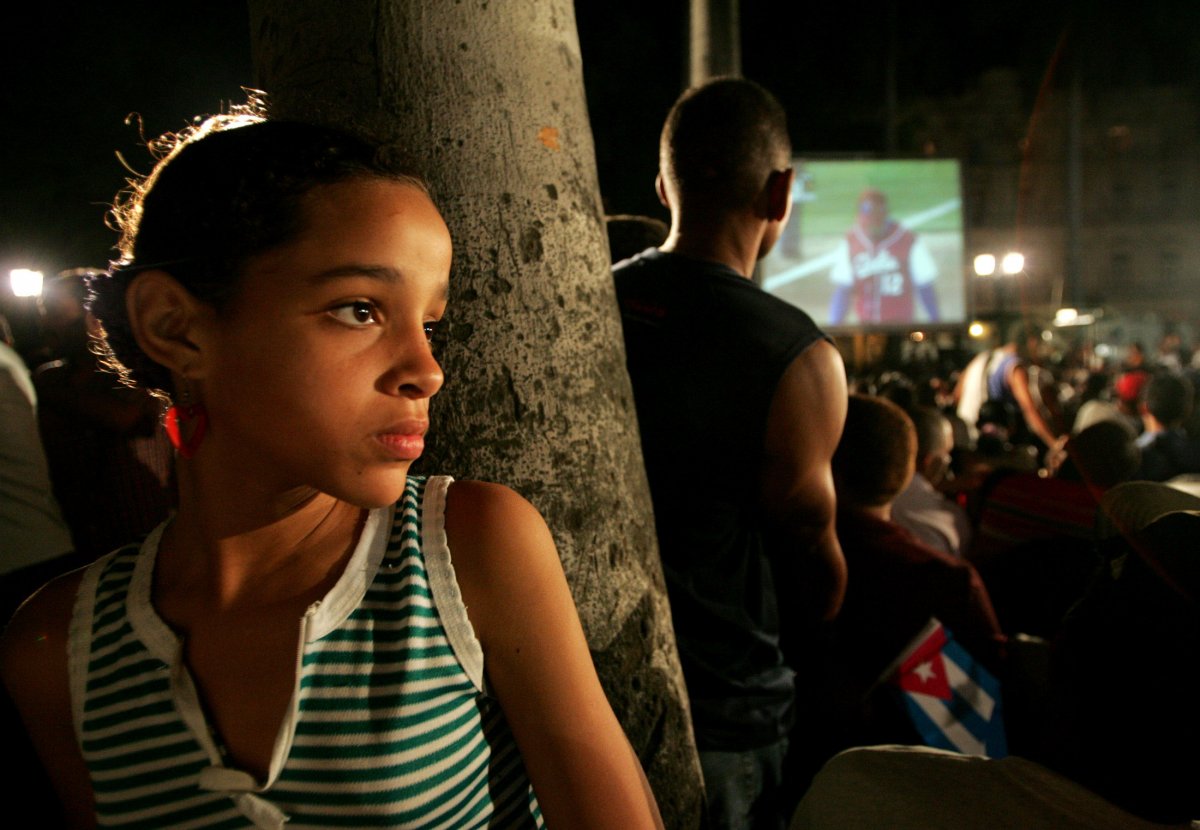 a-girl-leans-against-a-tree-in-havana-while-a-group-has-gathered-nearby-to-watch-their-countrys-team-compete-in-the-world-baseball-classic